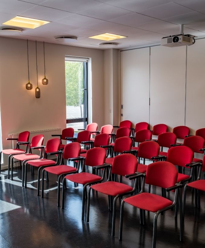 Lovise indrettet med røde konferencestole i biografopstilling og projektor til præsentationer og oplæg.