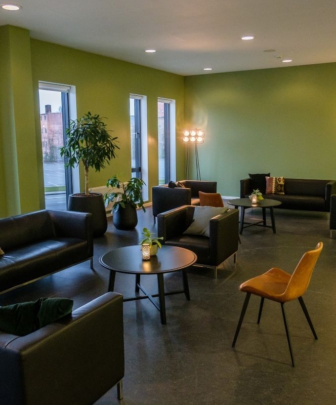 Moderne konferencecenter på Sjælland med loungeområde i Roskilde Kongres- og Idrætscenter Lyst loungeområde i Roskilde Kongres- og Idrætscenter på Sjælland med sofaer, stole og grønne planter – ideelt til pauser under konferencer.