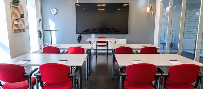 Roar indrettet med borde og røde stole i skolebordsopstilling foran en stor skærm. 
