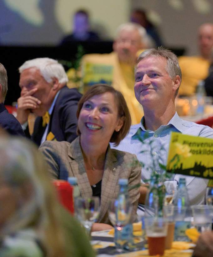 Smilende gæster sidder ved festdækkede borde under et firmaarrangement i Roskilde Kongres- og Idrætscenter med afslappet og hyggelig stemning.