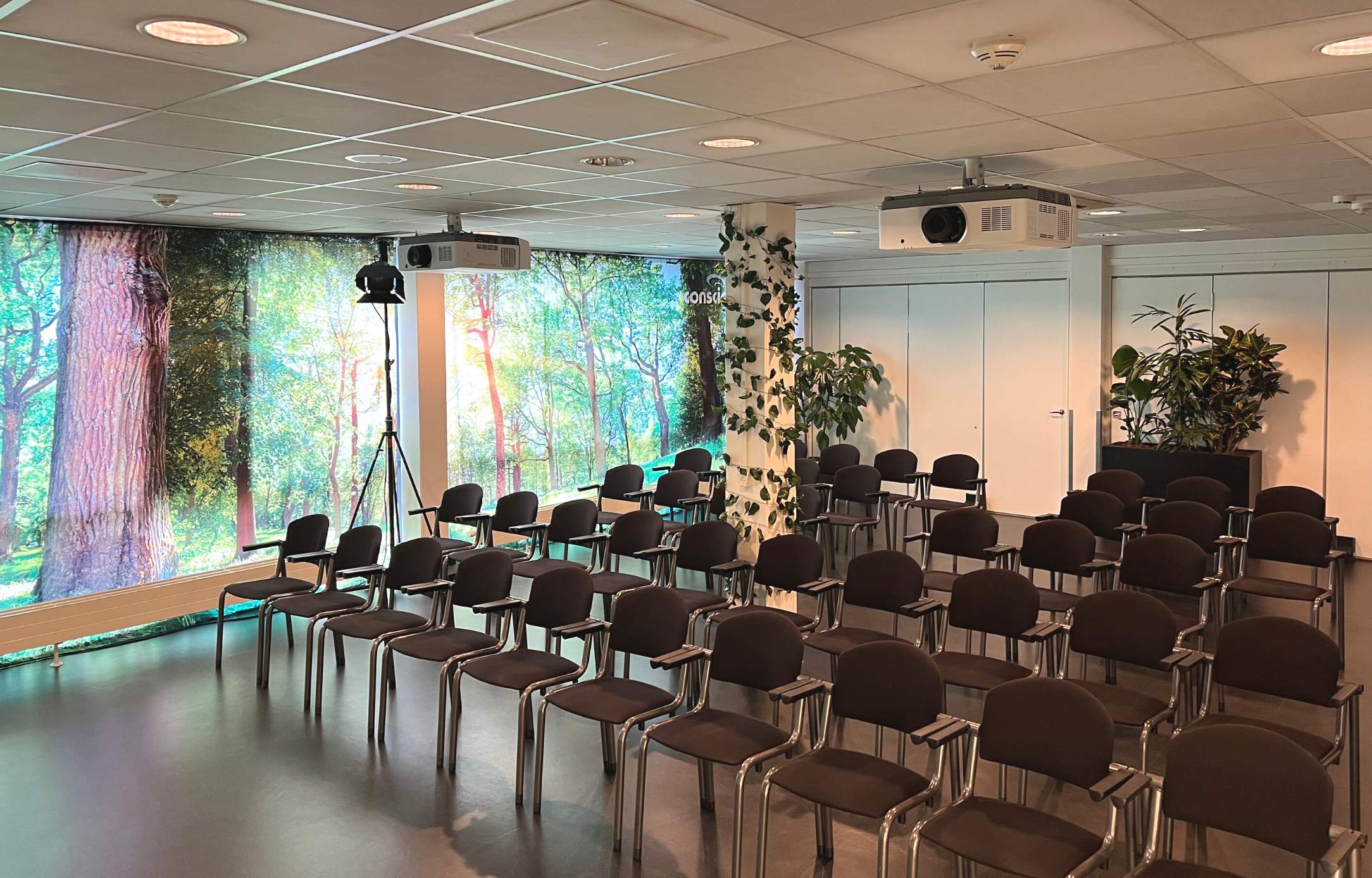 Konferencefaciliteter på Sjælland i Roskilde Kongres- og Idrætscenter Mødelokale i Roskilde Kongres- og Idrætscenter på Sjælland med stoleopsætning, projektorer og grønne detaljer, klar til konference eller seminar.