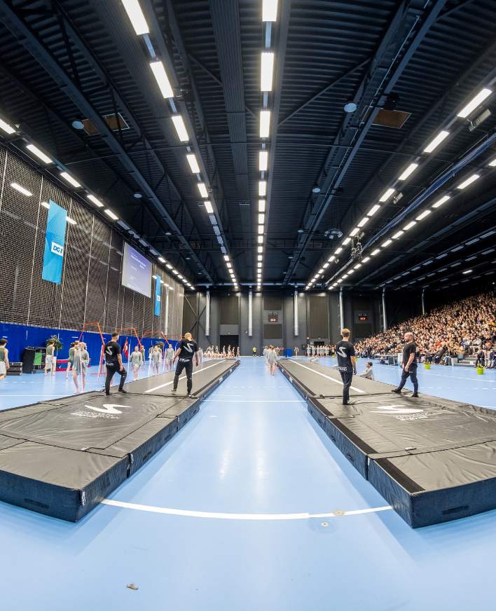 Gymnaster springer på to airtracks foran en fyldt tribune i en stor sportshal