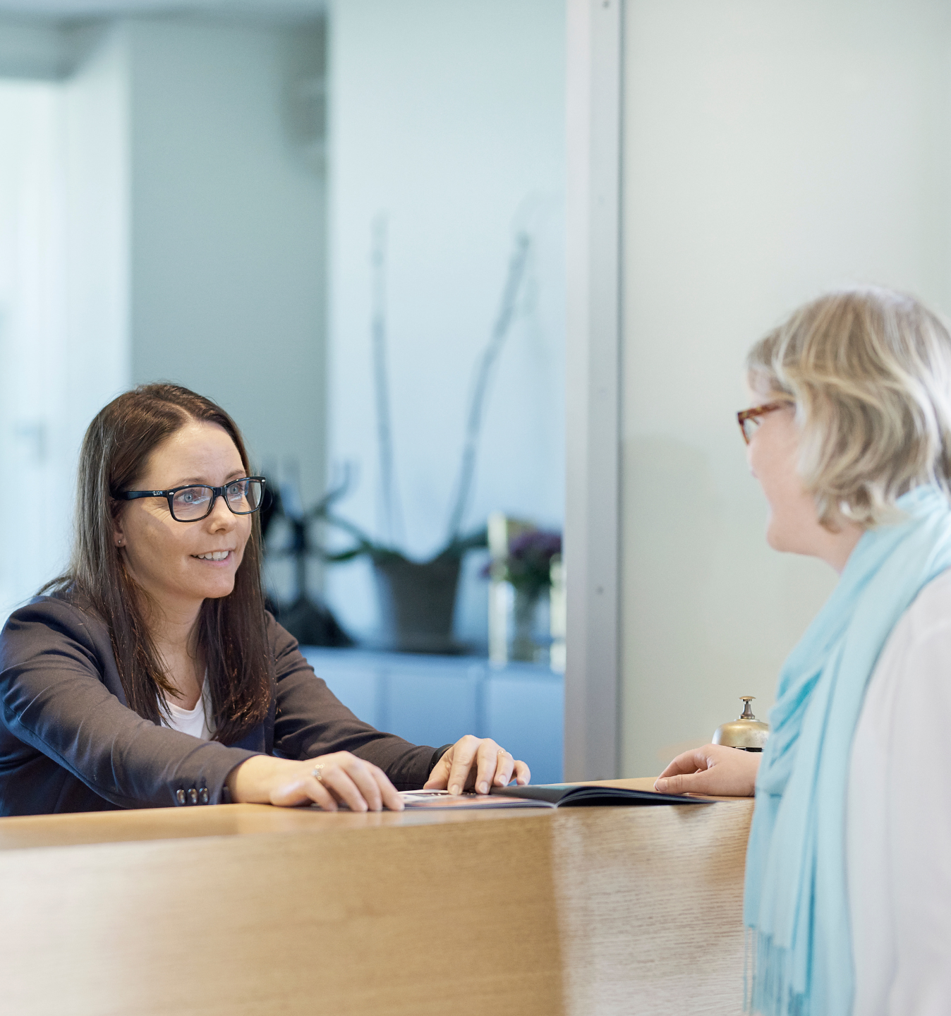 En medarbejder hjælper en gæst i receptionen i Roskilde Kongres- og Idrætscenter. Billedet viser den personlige kontakt og service, som er en del af hverdagen i huset.