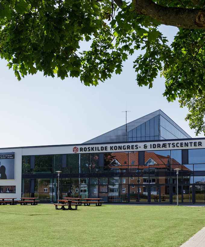 Grøn plæne og træer foran Roskilde Kongres- og Idrætscenters bygninger.