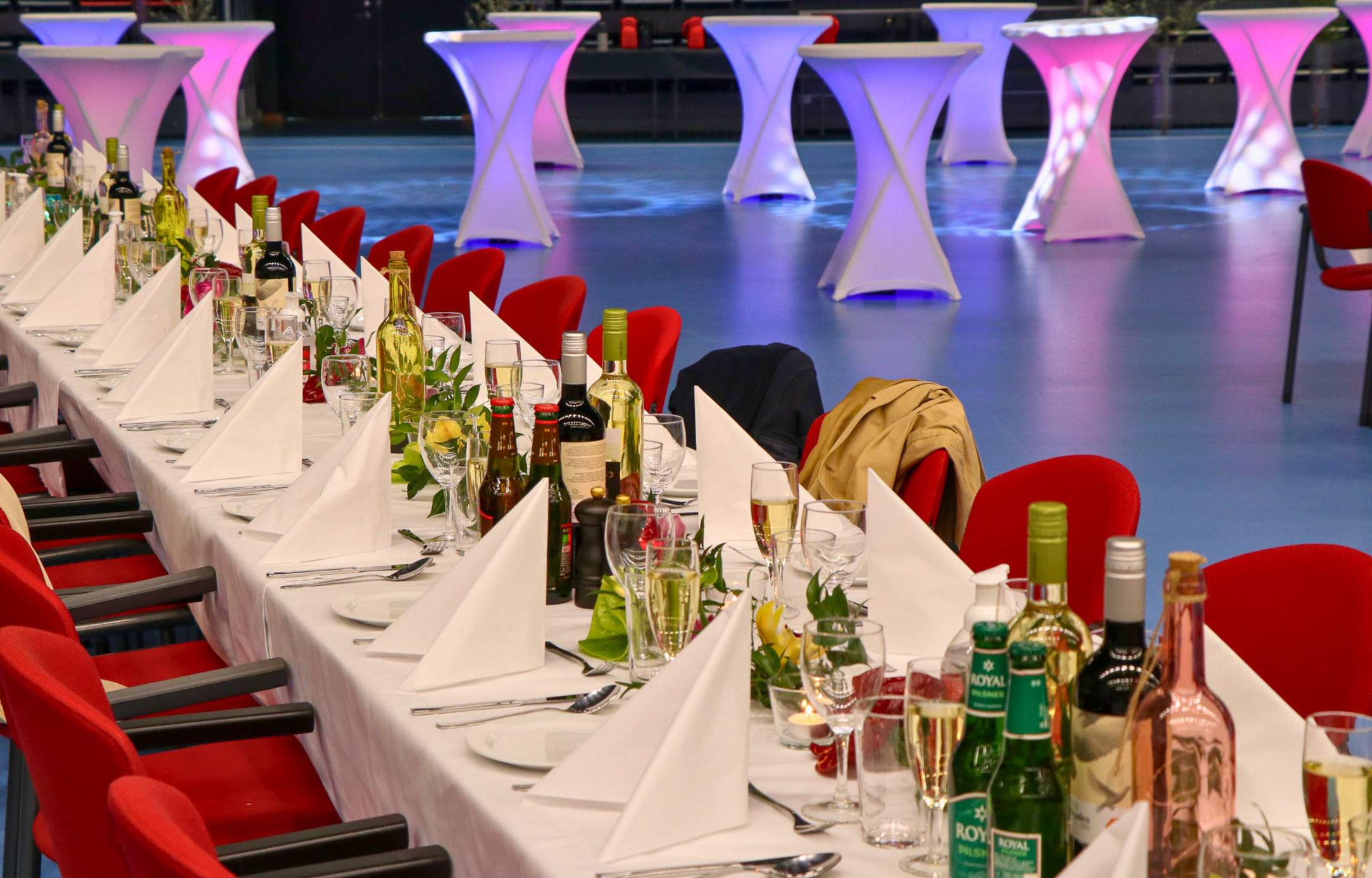 Langt festdækket bord med hvide duge, foldede servietter, vin og vandflasker, klar til en firma sommerfest i Roskilde Kongres- og Idrætscenter.