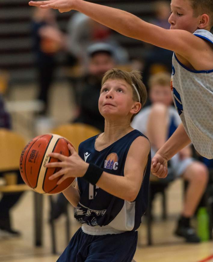 Ung basketballspiller med bolden mellem to modspillere under en kamp