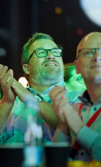 Engageret publikum under inspirerende konference i Roskilde Kongrescenter. Mand smiler og klapper under en konference i Roskilde Kongres- og Idrætscenter på Sjælland, hvor deltagerne nyder oplæg og fællesskab.