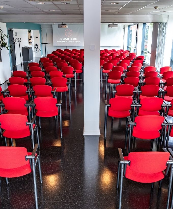 Maglekilde indrettet med røde konferencestole i biografopstilling foran lærred og projektor.