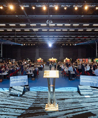 Konferencecenter på Sjælland med plads til store erhvervsarrangementer Stor konferencesal i Roskilde Kongres- og Idrætscenter på Sjælland set fra scenen, med talerstol, lysopsætning og hundredevis af deltagere ved runde borde.