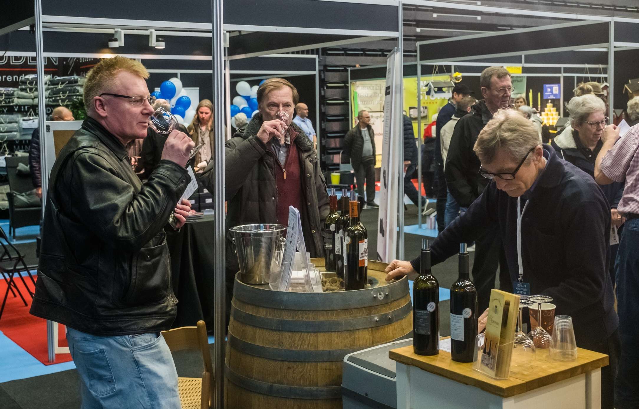 Vinstand med smagsprøver på messe i Roskilde Kongres- og Idrætscenter Besøgende nyder vinsmagning ved en udstillingsstand på messe i Roskilde Kongres- og Idrætscenter, hvor lokale og internationale produkter præsenteres.