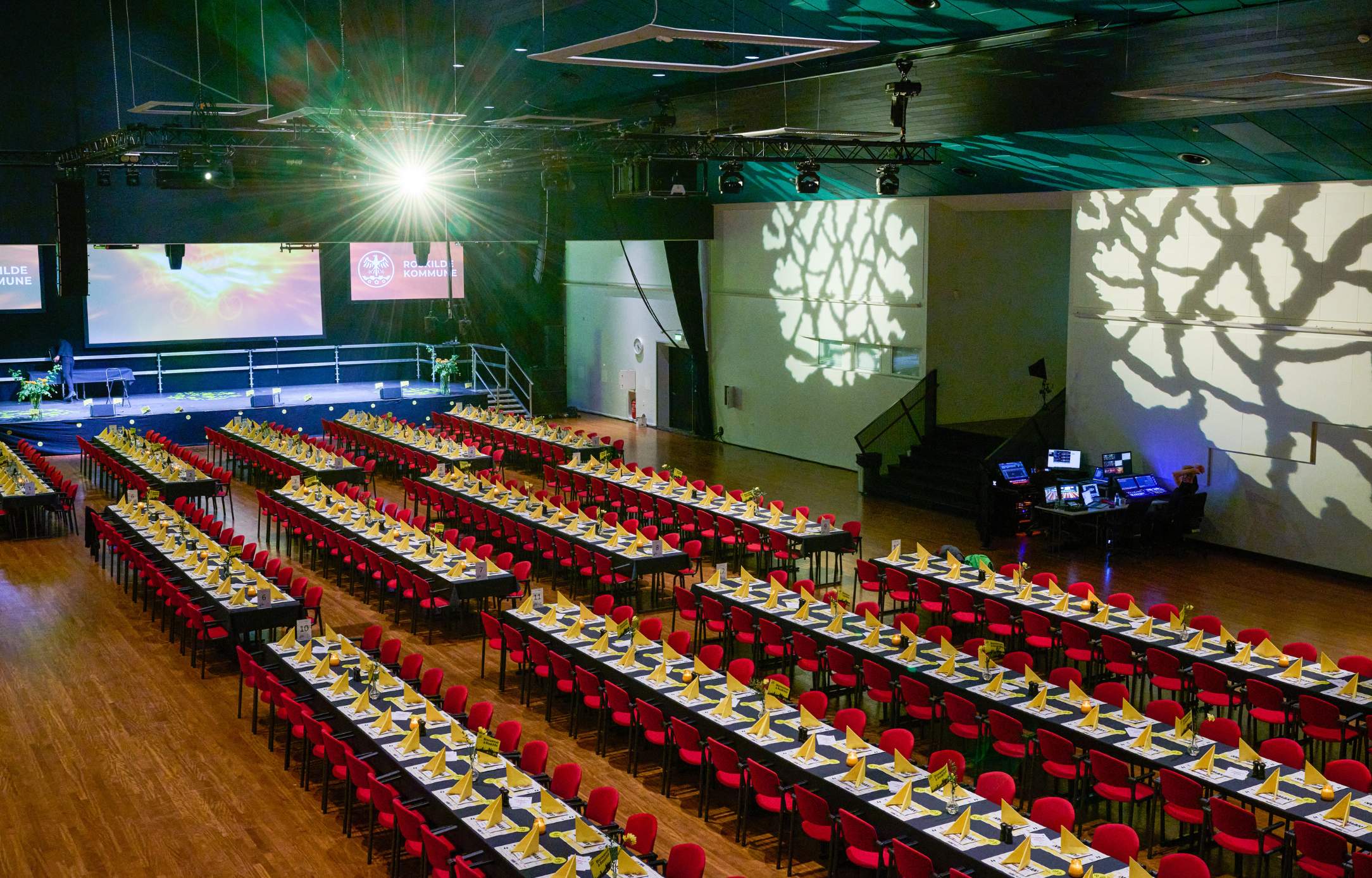 Langborde, røde stole og scenelys, der kaster dekorative mønstre på væggen.