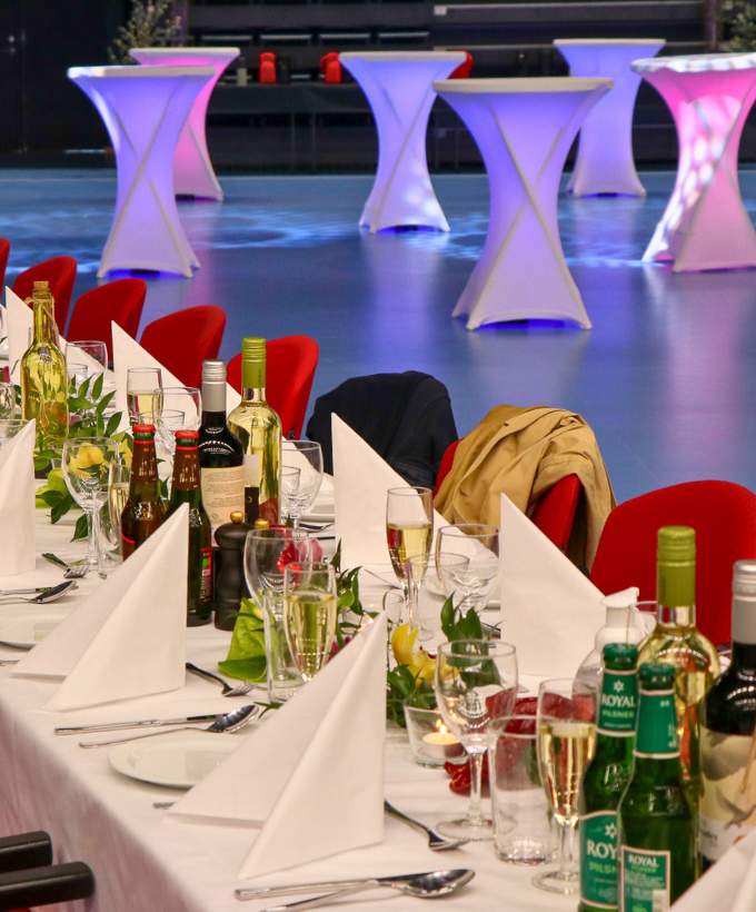 Langt festdækket bord med hvide duge, foldede servietter, vin og vandflasker, klar til en firma sommerfest i Roskilde Kongres- og Idrætscenter.