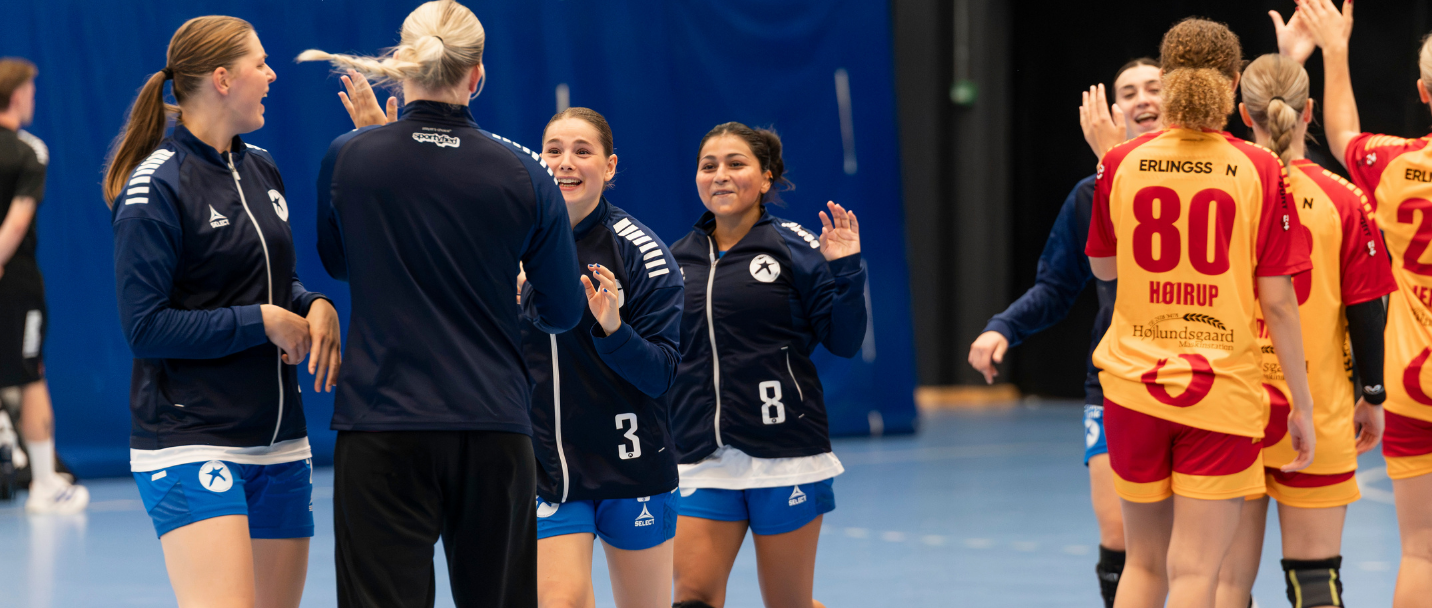 Håndboldspillere i hvid og blå samles på sidelinjen under en kvindehåndboldkamp i Roskilde Kongres- og Idrætscenter.