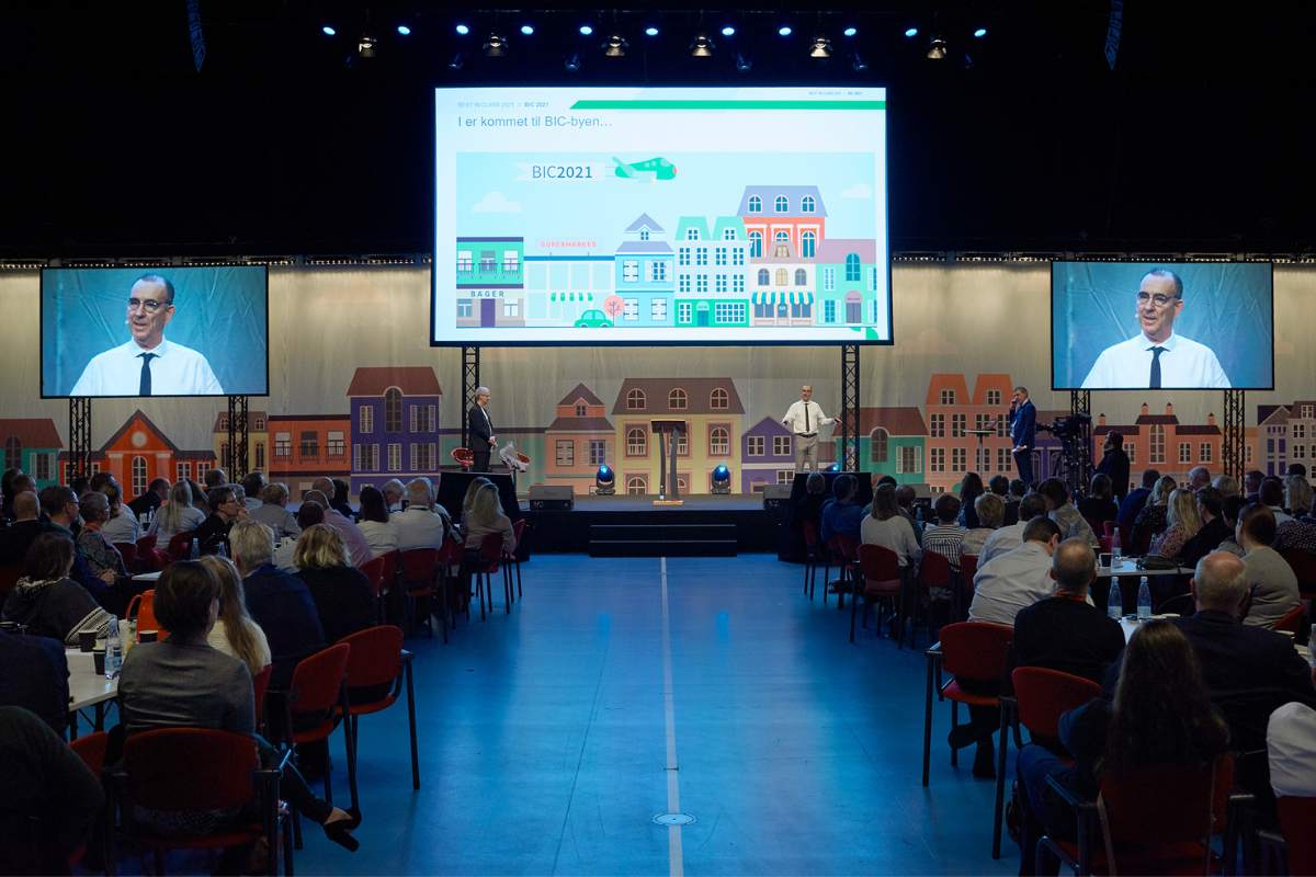Konference i Hal D med scene, storskærme og deltagere ved borde