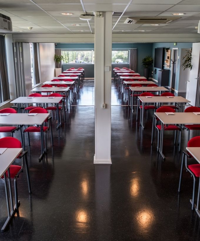 Maglekilde indrettet med borde og røde stole i skolebordsopstilling med god plads til deltagere og oplæg.