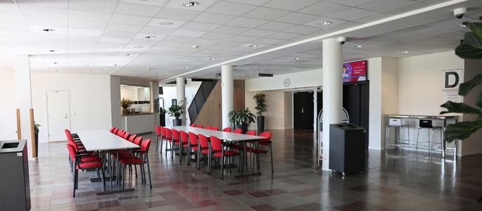 Foyer Øst i Roskilde Kongres- og Idrætscenter med borde og røde stole, åbne opholdsarealer og adgang til husets øvrige faciliteter. 