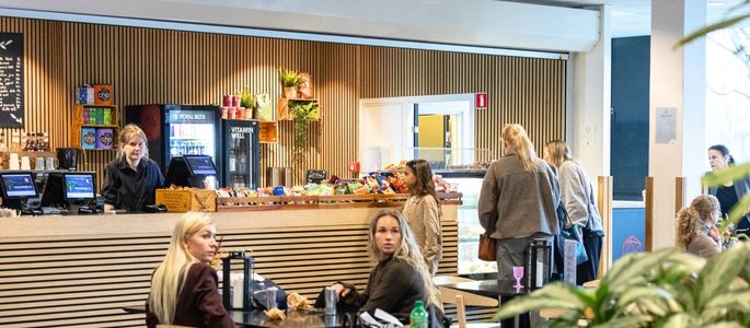  Lyst caféområde med siddepladser, grønne planter og kaffebar i Roskilde Kongres- og Idrætscenter.