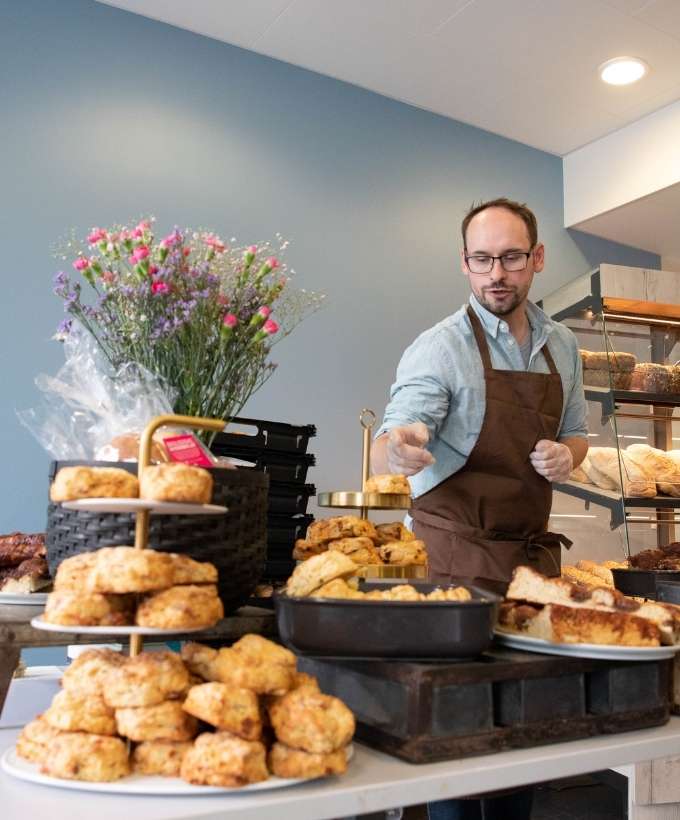 Bagerstand med frisk brød og kager på messe i Roskilde Kongres- og Idrætscenter Udstiller præsenterer friskbagt brød og kager på en messe i Roskilde Kongres- og Idrætscenter, hvor besøgende kan smage og købe lokale specialiteter.