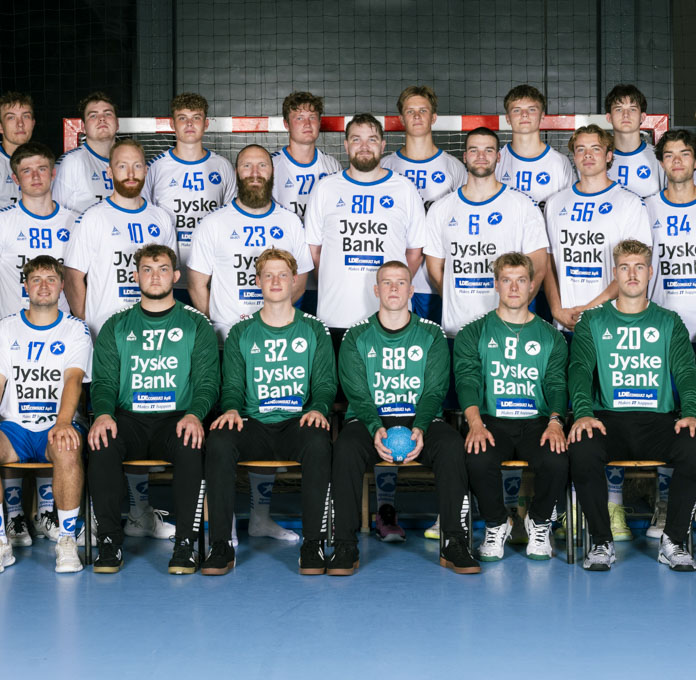Spillere, målmænd og trænere samlet til holdbillede foran et håndboldmål i Roskilde Kongres- og Idrætscenter. 